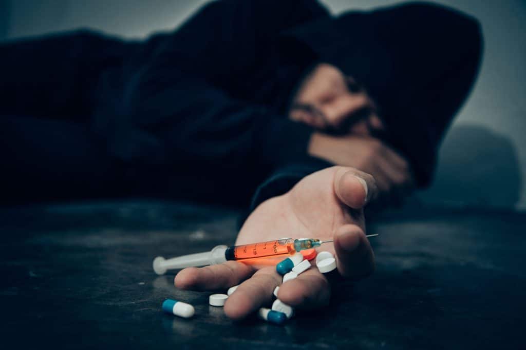 man lying on the floor with pills and syringe on hand