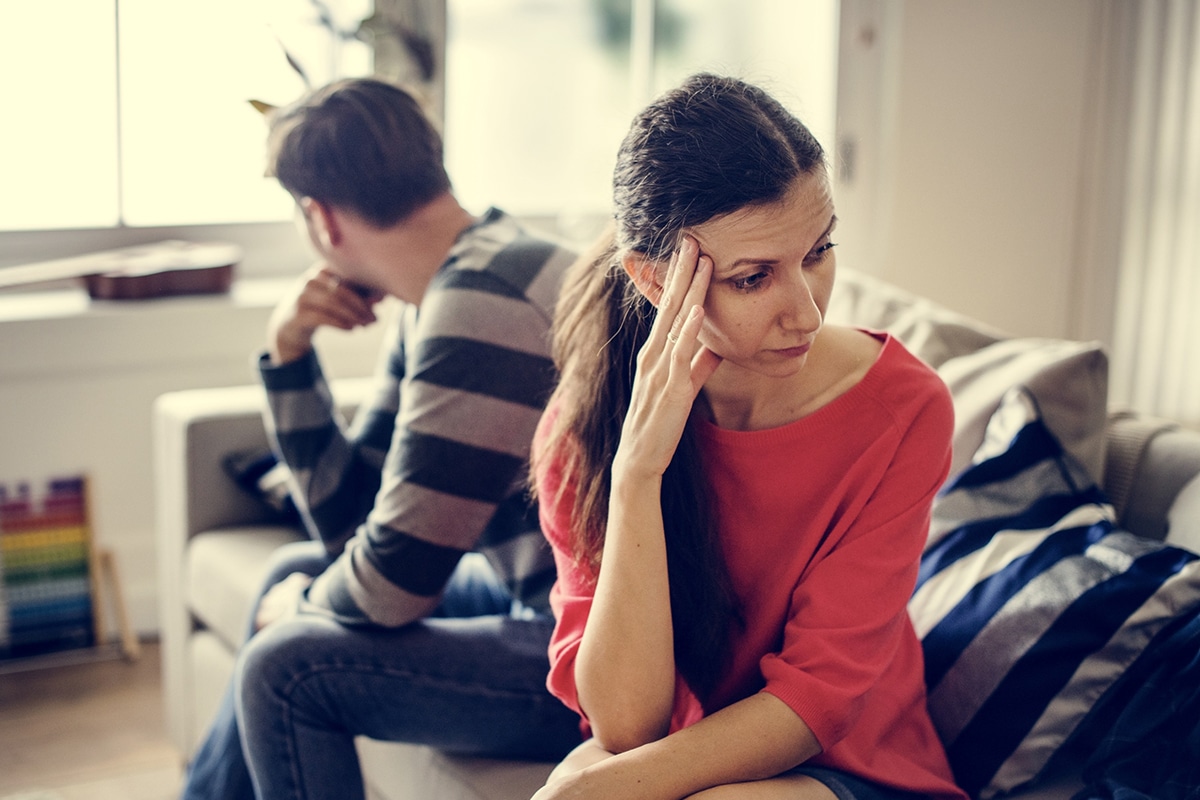 A couple sits on a sofa, unable to connect because their experiences in a foreign country are so different