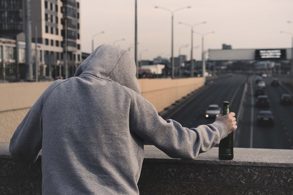 Man in hooded sweater holding an alcoholic beverage on the bridge