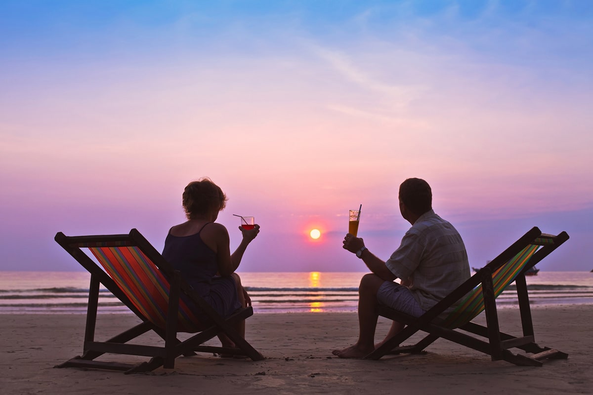 A retired couple have cocktails as they watch a tropical sunset.