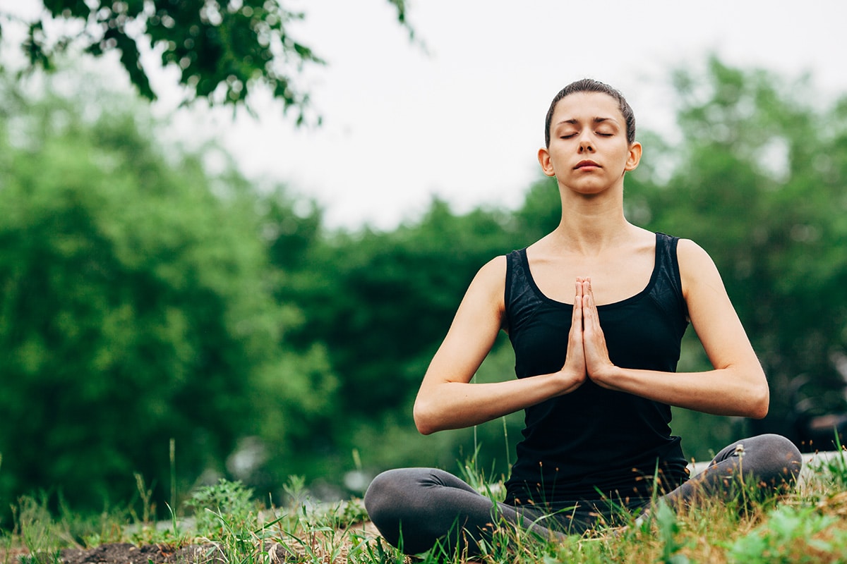  a woman is doing holistic meditation on a green field.