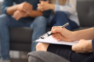 A hand holding a fillout form on a clipboard while a couple in the background hold hands