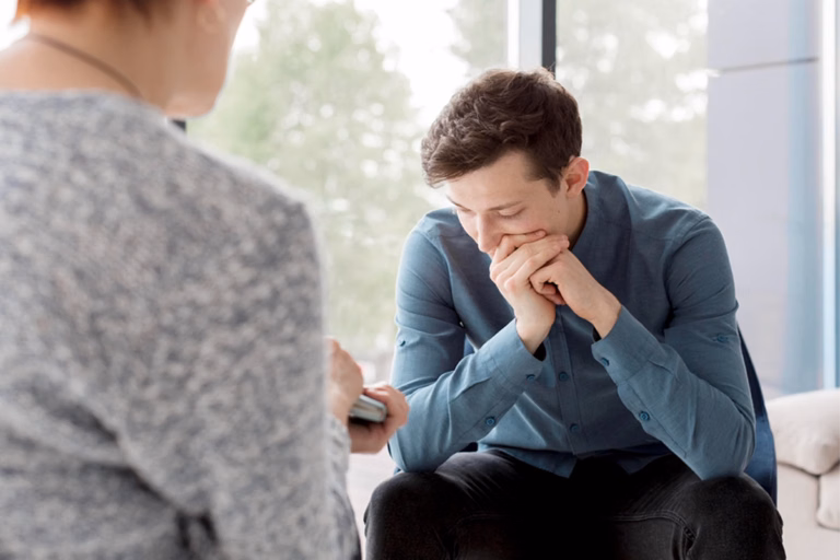Young man with clasped hands talking with a therapist during a trauma therapy session